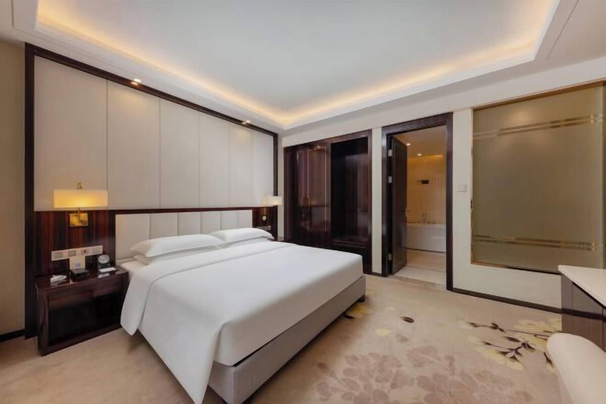 A hotel room with a large bed, bedside tables, a desk, and a wardrobe.