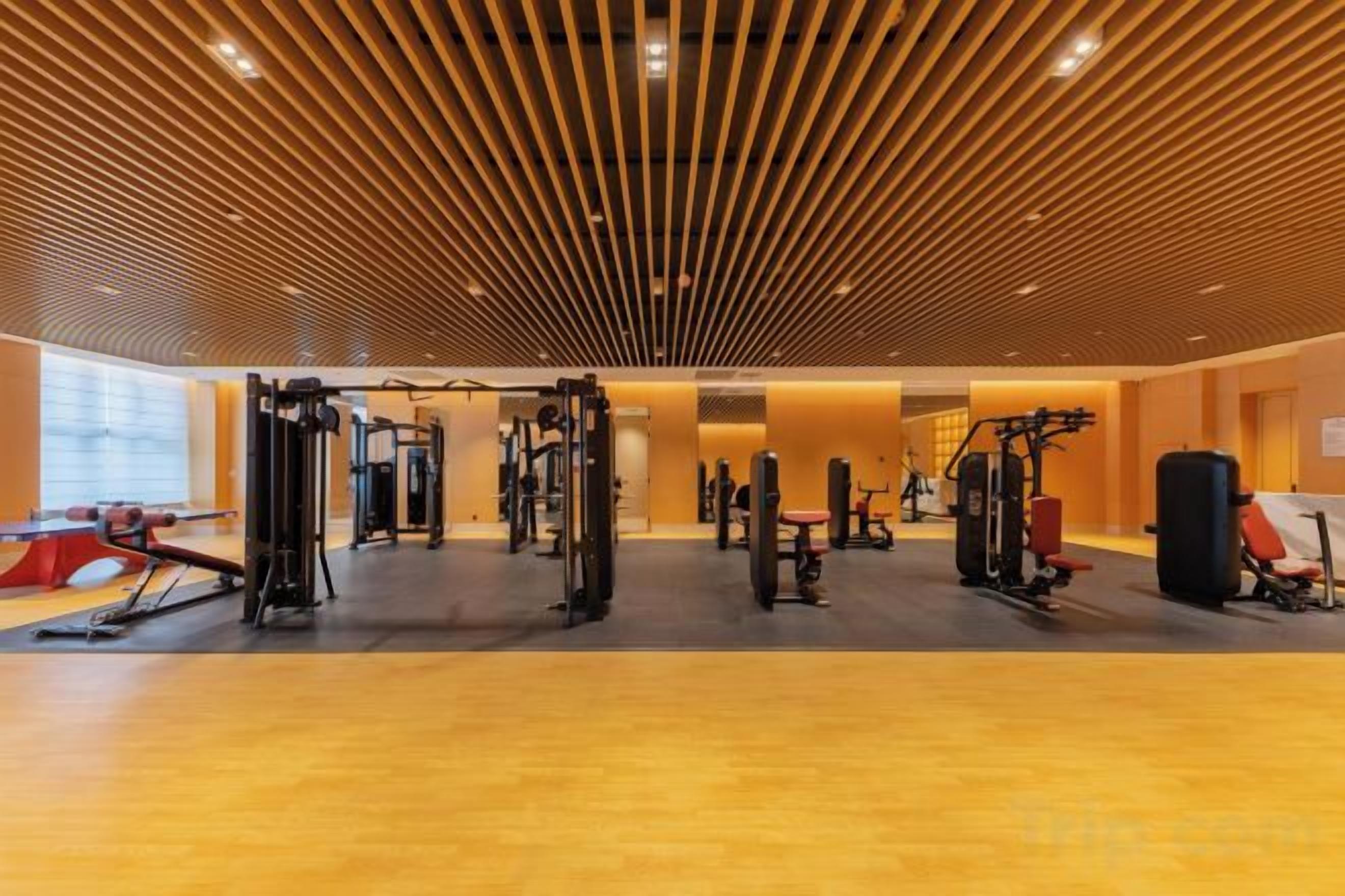 A gym with various exercise equipment, a wooden ceiling, and a large window.