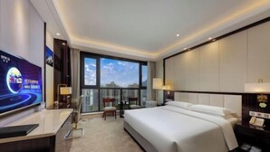 Camera d'albergo moderna con un letto grande, una scrivania con televisore a schermo piatto, una piccola area salotto e un'ampia finestra con vista sulla città.