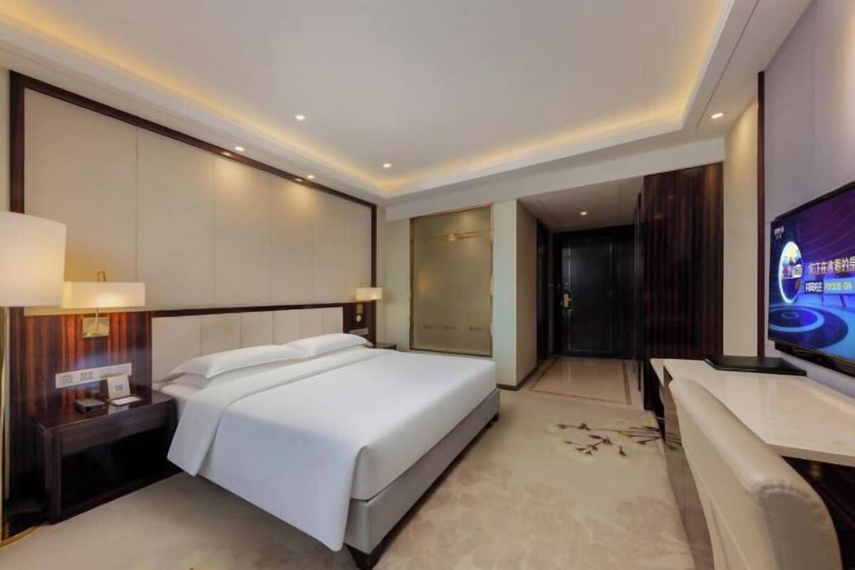 A modern hotel room with a large bed, bedside tables, a TV, and a seating area.