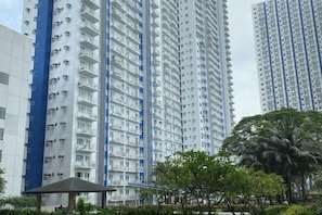 A high-rise residential building with multiple balconies, a covered pavilion, and surrounding greenery.