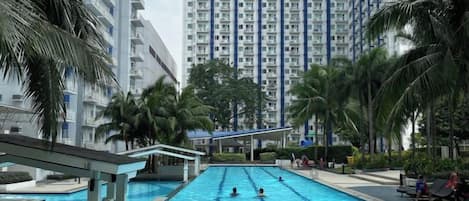 Piscina rodeada por edifícios residenciais altos, palmeiras e uma galeria coberta.