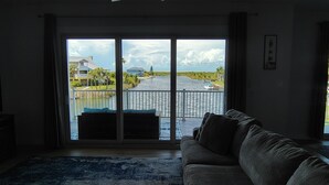 A living room with a large sliding glass door leading to a balcony overlooking a body of water, a ceiling fan, and a blue patterned rug. - Waterfront and Gulfview Retreat Hernando Beach (Hernando Beach)