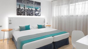 Ett modernt hotellrum med en stor säng, två sängbord, ett litet runt bord och utsikt över havet genom tunna gardiner.