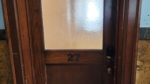Een houten deur met een geëtste ruit en het nummer 27.