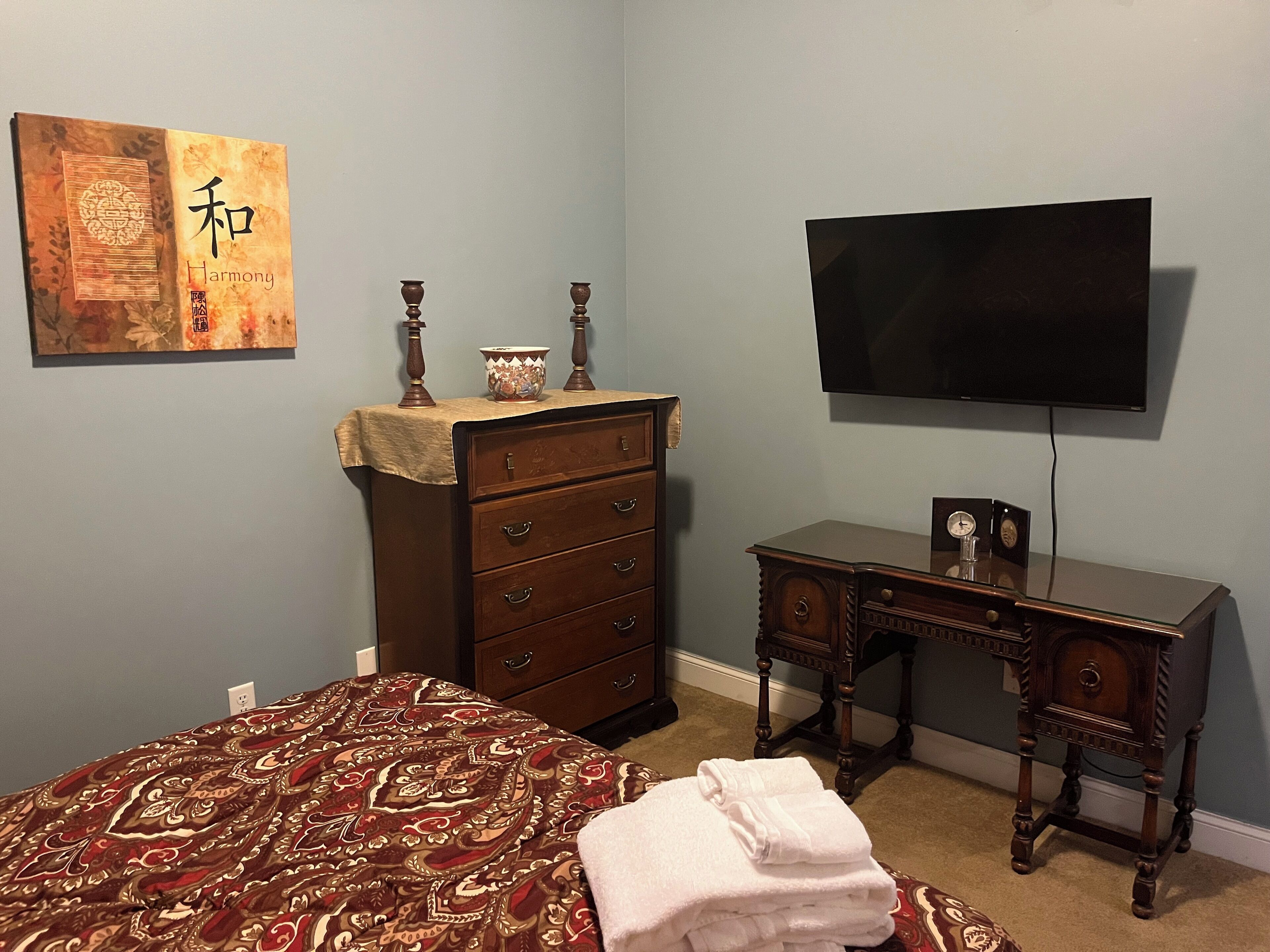 Un dormitorio con cama, cómoda, escritorio y televisor en la pared.