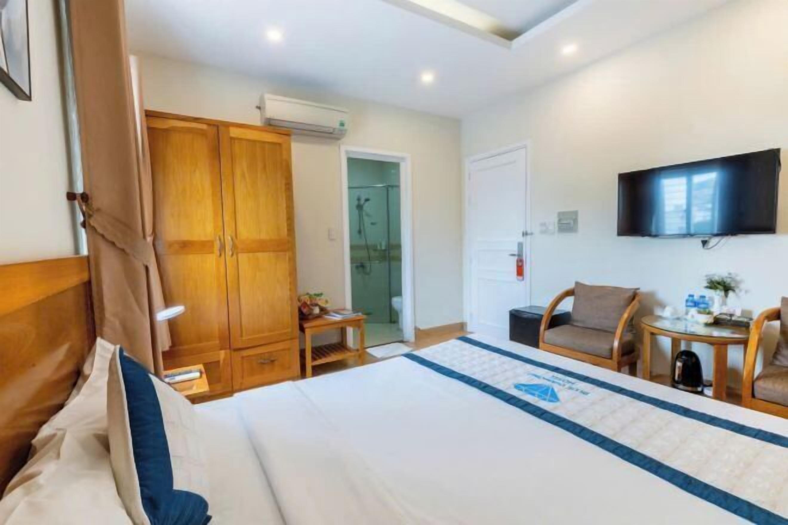 Une chambre d’hôtel avec un lit, une armoire en bois, une télévision et une petite table avec une chaise.