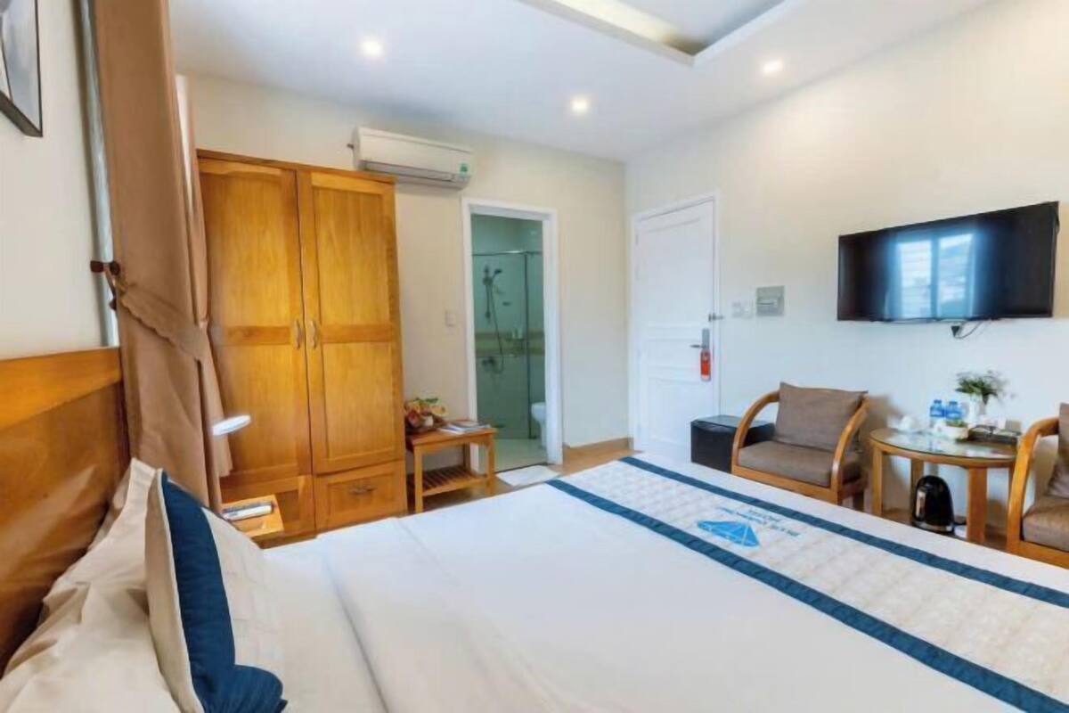 Une chambre d’hôtel avec un lit, une armoire en bois, une télévision et une petite table avec une chaise.