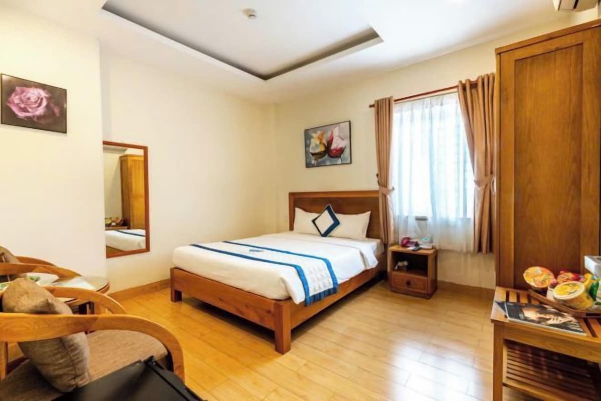 Una camera da letto con un letto di legno, un comodino, una sedia, uno specchio e una finestra con tende.