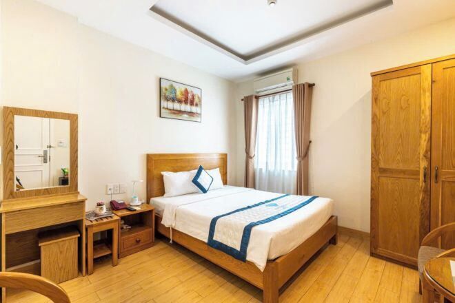 Une chambre d’hôtel avec un lit en bois, un bureau avec une chaise, une armoire et une fenêtre avec des rideaux.
