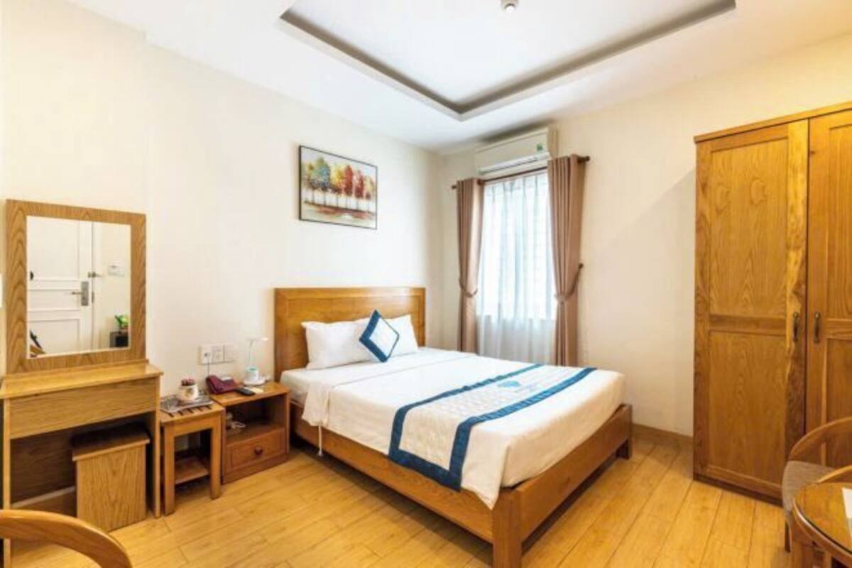 Une chambre d’hôtel avec un lit en bois, un bureau avec une chaise, une armoire et une fenêtre avec des rideaux.