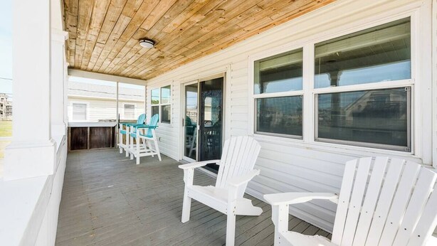 Eine überdachte Veranda mit weißen Adirondack-Stühlen, einem Tisch und Blick auf den Ozean.
