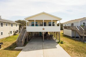 A two-story building with a covered front porch and a small outdoor seating area. - Beach getaway! Walk to beach, hot tub, near shops (Nags Head)
