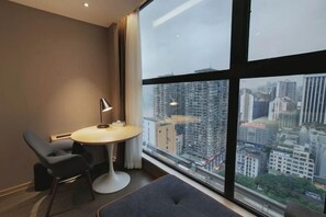 A modern hotel room with a large window, a round table, a chair, and a small sofa.
