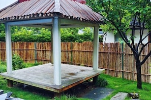 Un belvédère doté d’un toit en tuiles, entouré d’une clôture en bambou, avec un arbre en premier plan.