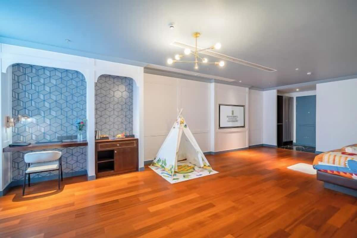 A modern living room with a wooden floor, a white sofa, a desk with a chair, a tent, and a chandelier.