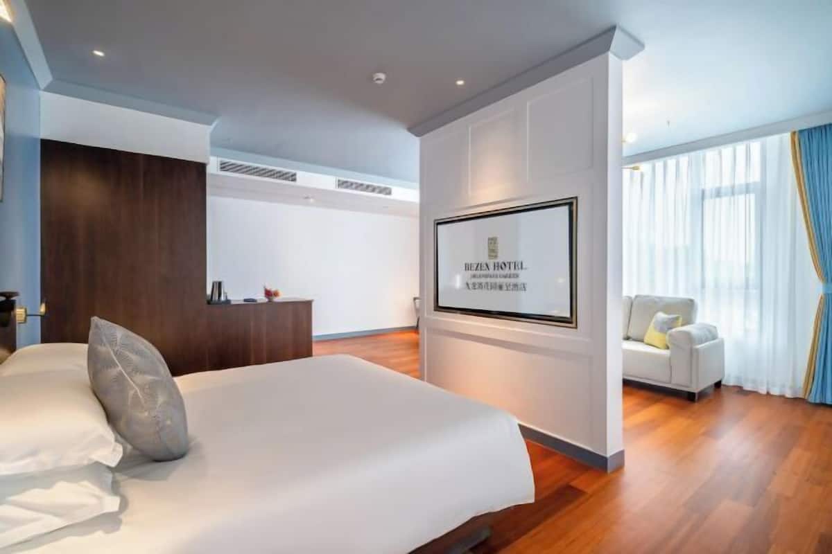 A hotel room with a bed, a TV mounted on the wall, a sofa, and a large window with curtains.