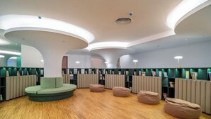 Una biblioteca moderna con luminarias de techo curvas, suelo de madera y zonas de estar en tonos verde y beige.