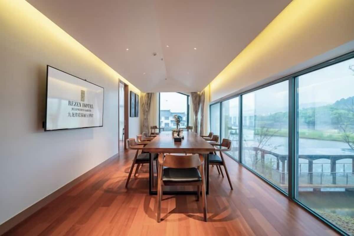 A modern hotel room with a large dining table, comfortable seating, and large windows offering a view of the outdoors.