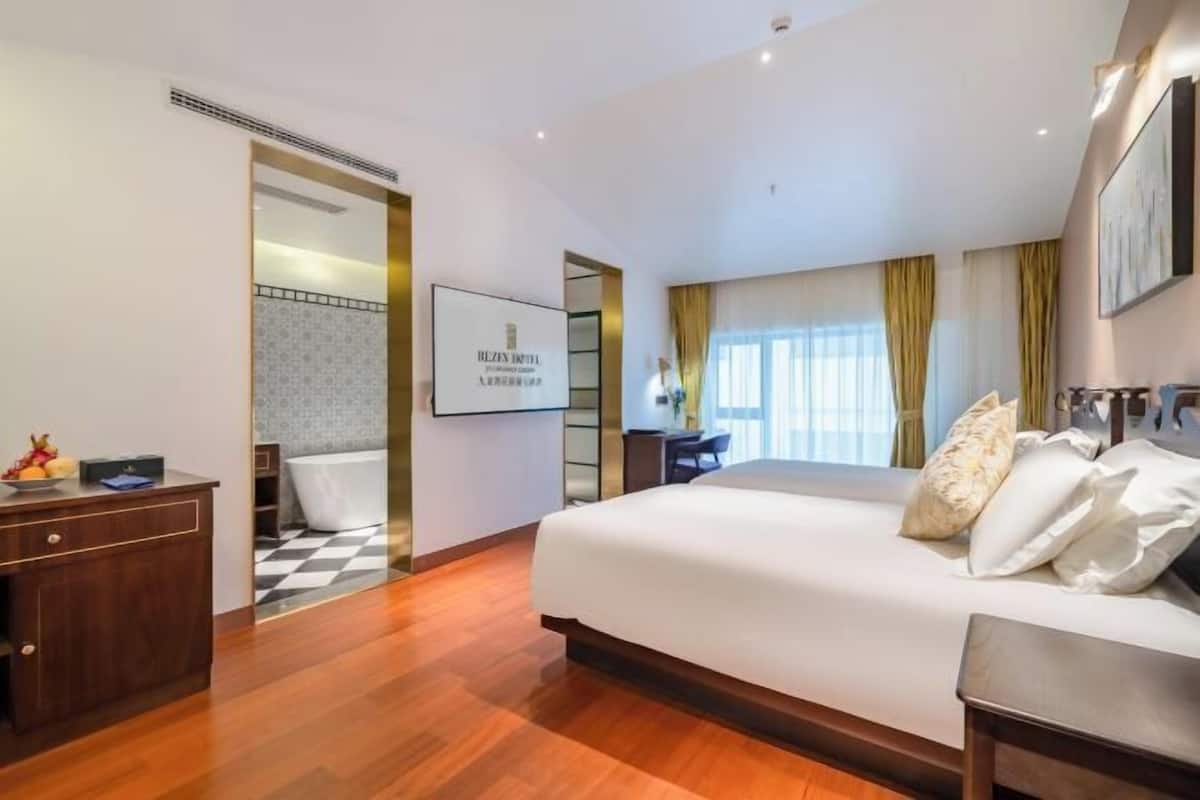 A hotel room with a large bed, a desk, a chair, a wardrobe, and a bathroom visible through an open door.