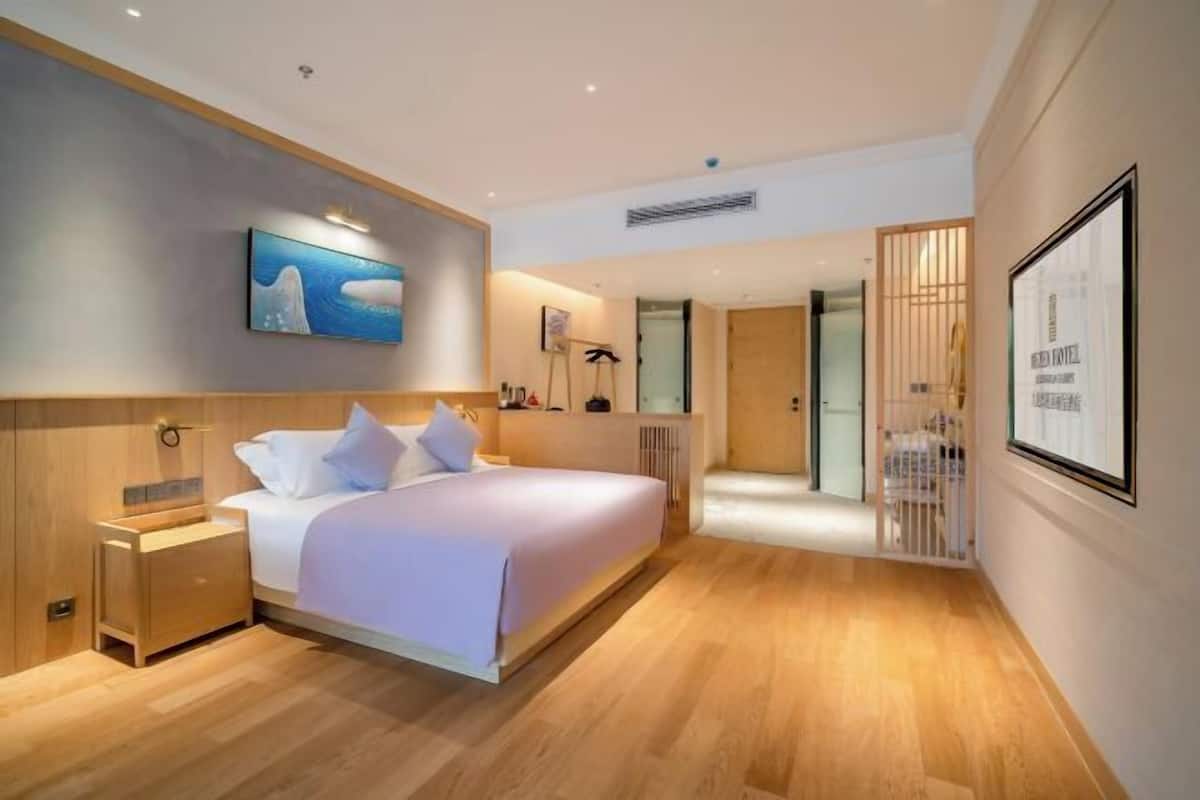 A modern hotel room with a large bed, wooden flooring, a painting on the wall, and a framed picture.