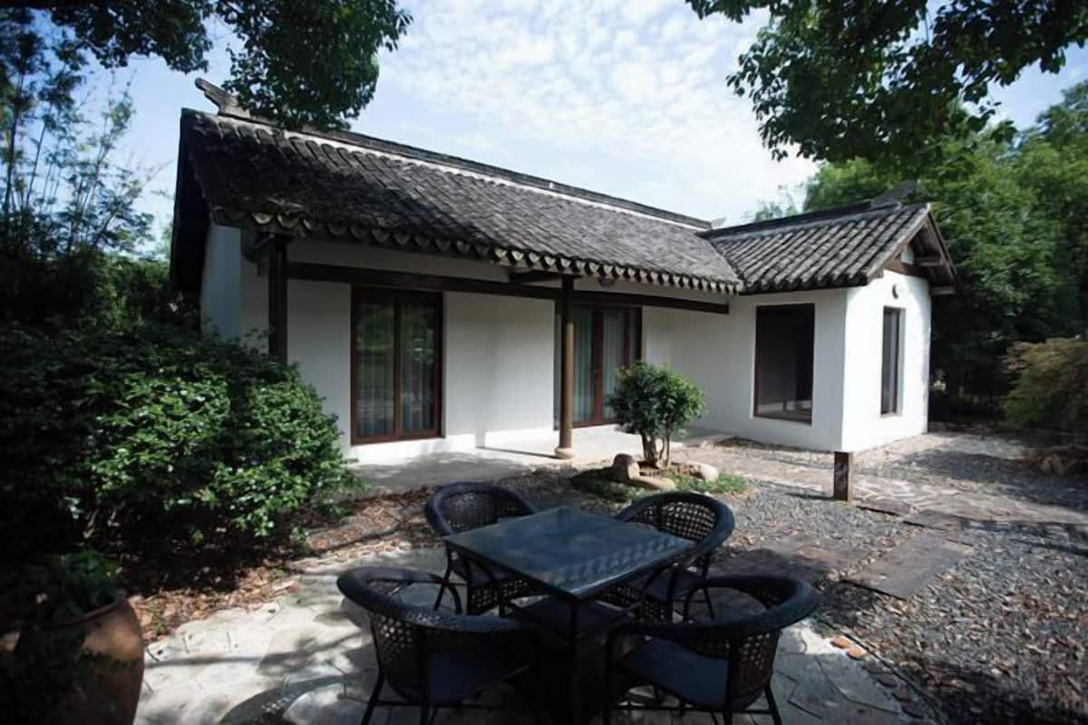 A traditional-style building with a tiled roof, a small garden with a table and chairs, and a potted plant.