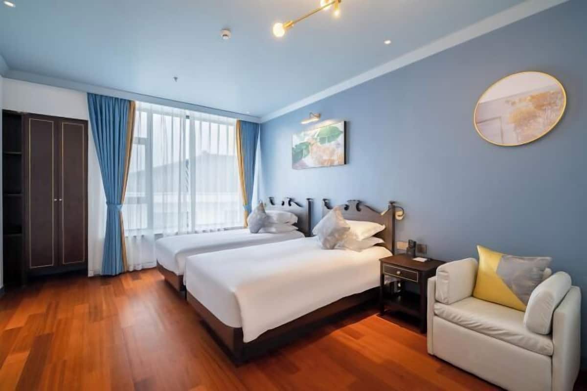 A hotel room with two beds, a sofa, a desk, and a large window with curtains.