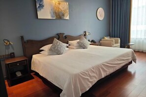 Une chambre d’hôtel avec un grand lit, une table de chevet avec une lampe, une petite table d’appoint, une chaise et une grande fenêtre avec des rideaux.