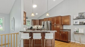 Une cuisine moderne avec des meubles en bois, un réfrigérateur en acier inoxydable et un coin bar doté de tabourets blancs.