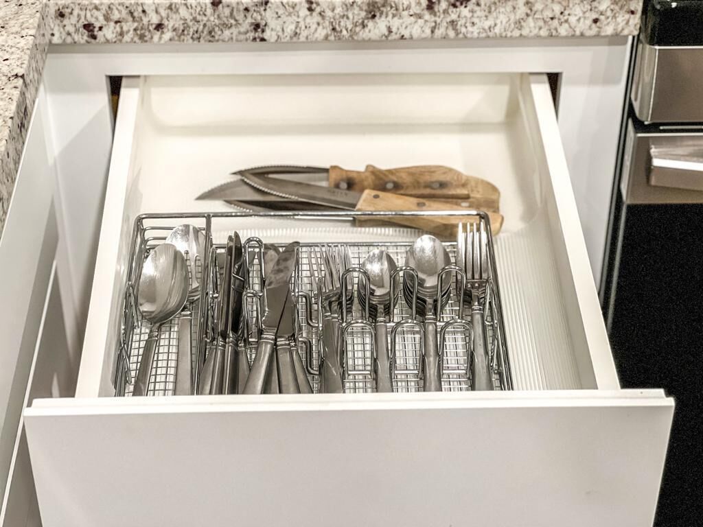 A drawer with a utensil organizer containing spoons, forks, and knives.