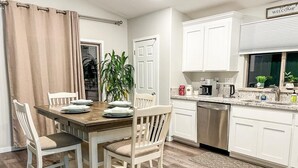 A dining area with a wooden table and white chairs, a kitchen with white cabinets, and a window with a view. - ROSEVILLE GETAWAY (Roseville)