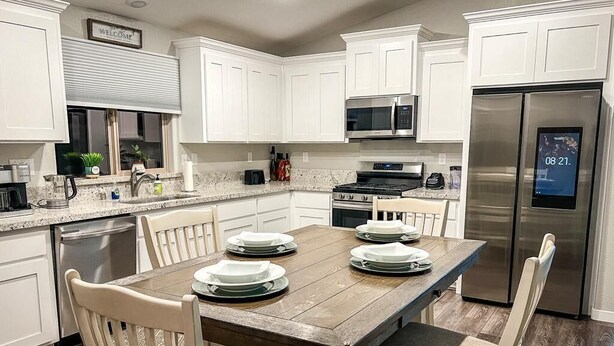 A kitchen with white cabinets, a wooden dining table, and a stainless steel refrigerator. - ROSEVILLE GETAWAY (Roseville)