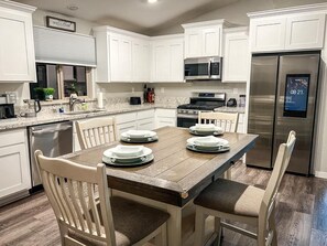 A kitchen with white cabinets, a wooden dining table, and a stainless steel refrigerator. - ROSEVILLE GETAWAY (Roseville)