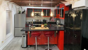 A modern kitchen with red cabinetry, stainless steel appliances, and pendant lighting.