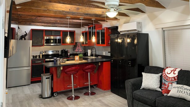 A modern kitchen with red and black cabinetry, a stainless steel refrigerator, and a built-in oven. There are two red bar stools and a black countertop.