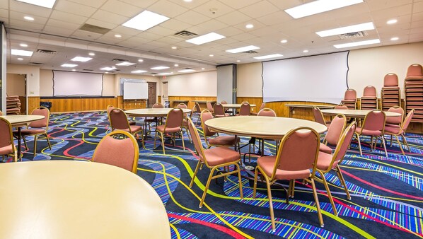 A conference room with round tables and chairs, a projector screen, and a carpeted floor.