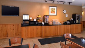 A hotel reception area with a wooden counter, coffee machines, a fruit bowl, and a clock on the wall.