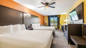 A hotel room with two beds, a ceiling fan, a TV, and a desk with a chair.