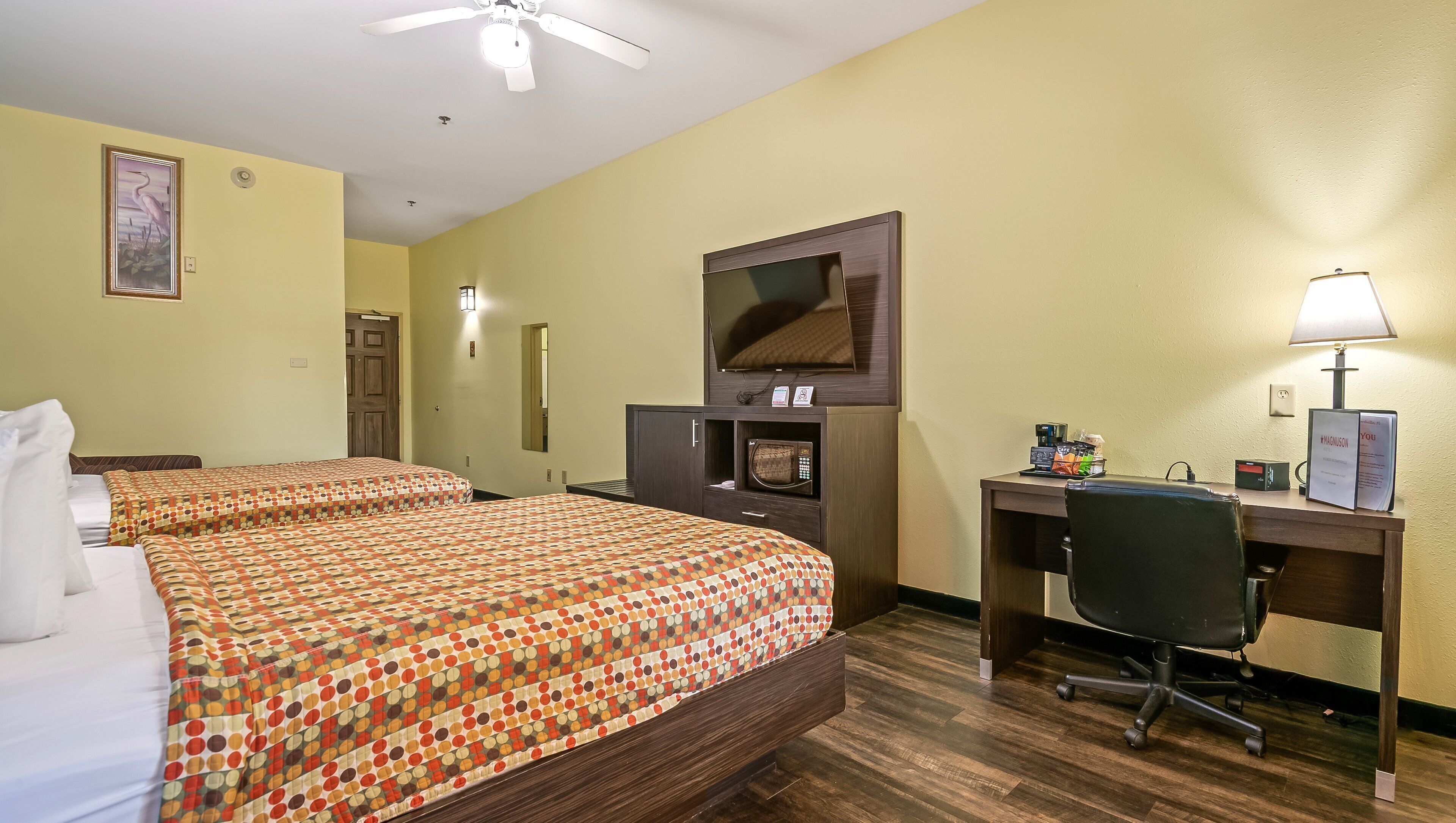 A hotel room with two beds, a desk, a chair, a TV, a microwave, and a coffee maker.