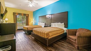 A hotel room with two beds, a desk, a chair, a ceiling fan, and a window with curtains.