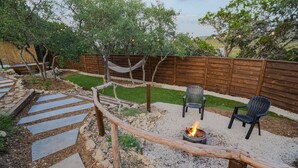 Ein Garten mit Feuerstelle, Gartenmöbeln, einer Hängematte und einem Kiesweg.