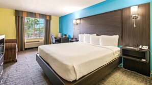 Une chambre d’hôtel avec un grand lit, un bureau, une chaise, une lampe de bureau, un téléphone et une fenêtre avec des rideaux.