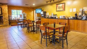C’est un restaurant avec des murs en bois et une cheminée en pierre. On y trouve des tables et des chaises, un téléviseur et une machine à café.