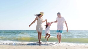 A family of three walking on a sandy beach with the ocean in the background. - Relax in Style: King Bed Non-Smoking Room at Wildwood Inn (Crawfordville)