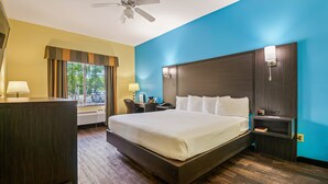 A hotel room with a large bed, a desk, a chair, a nightstand, a lamp, and a ceiling fan. - Relax in Style: King Bed Non-Smoking Room at Wildwood Inn (Crawfordville)