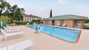 Una piscina rectangular con tabla de clavados, rodeada de sillas reclinables blancas y una zona de estar cubierta.