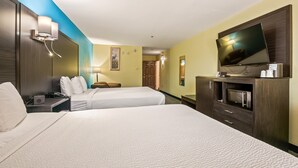 Une chambre d’hôtel avec deux lits, une télévision, un bureau avec un téléphone et une lampe.