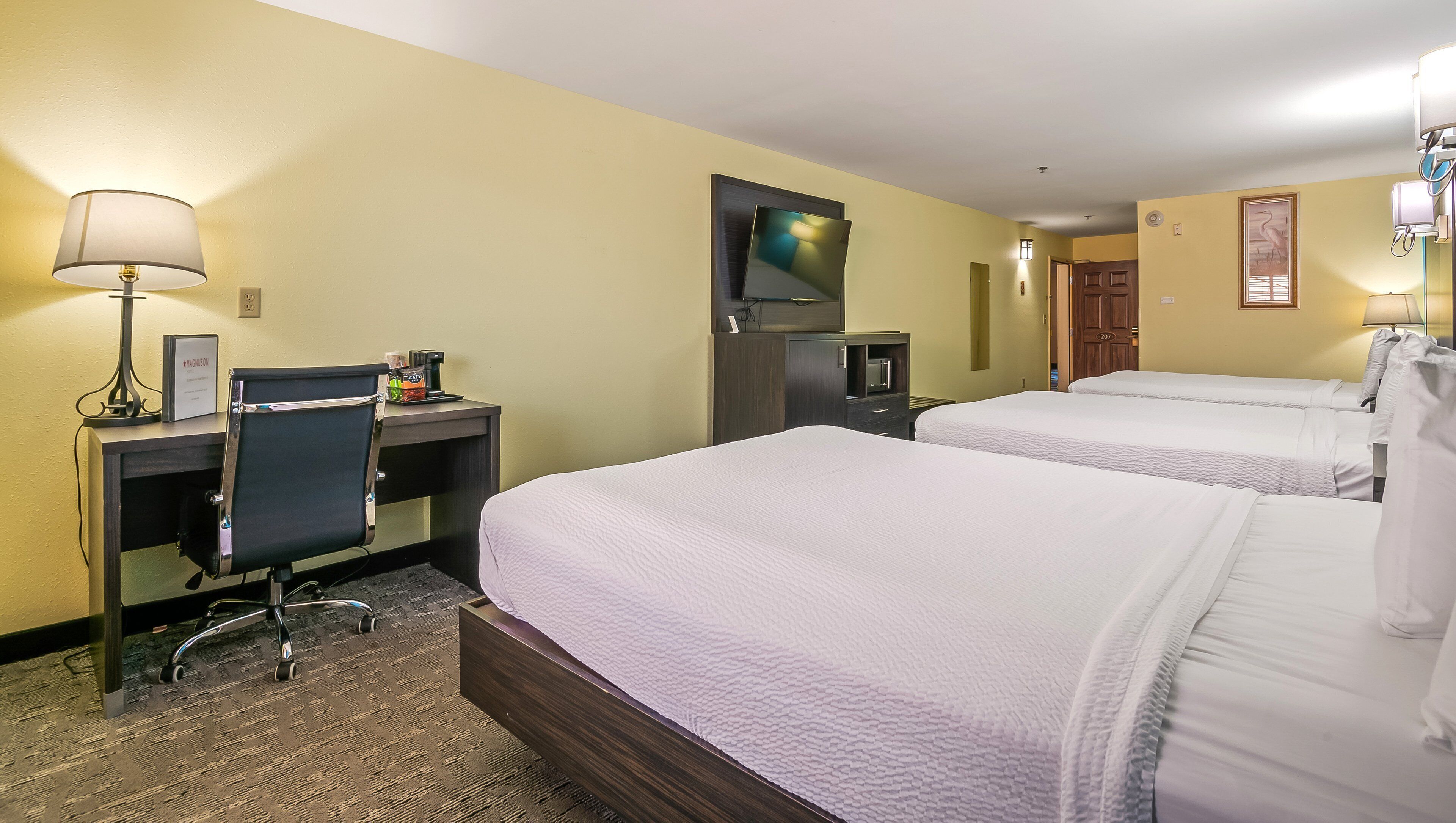 A hotel room with two beds, a desk with a chair, a TV, and a coffee machine.