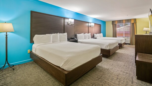 Quarto de hotel com duas camas, uma escrivaninha, uma luminária e uma janela com persianas.