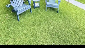 A courtyard with three Adirondack chairs, a small table, and a palm tree.